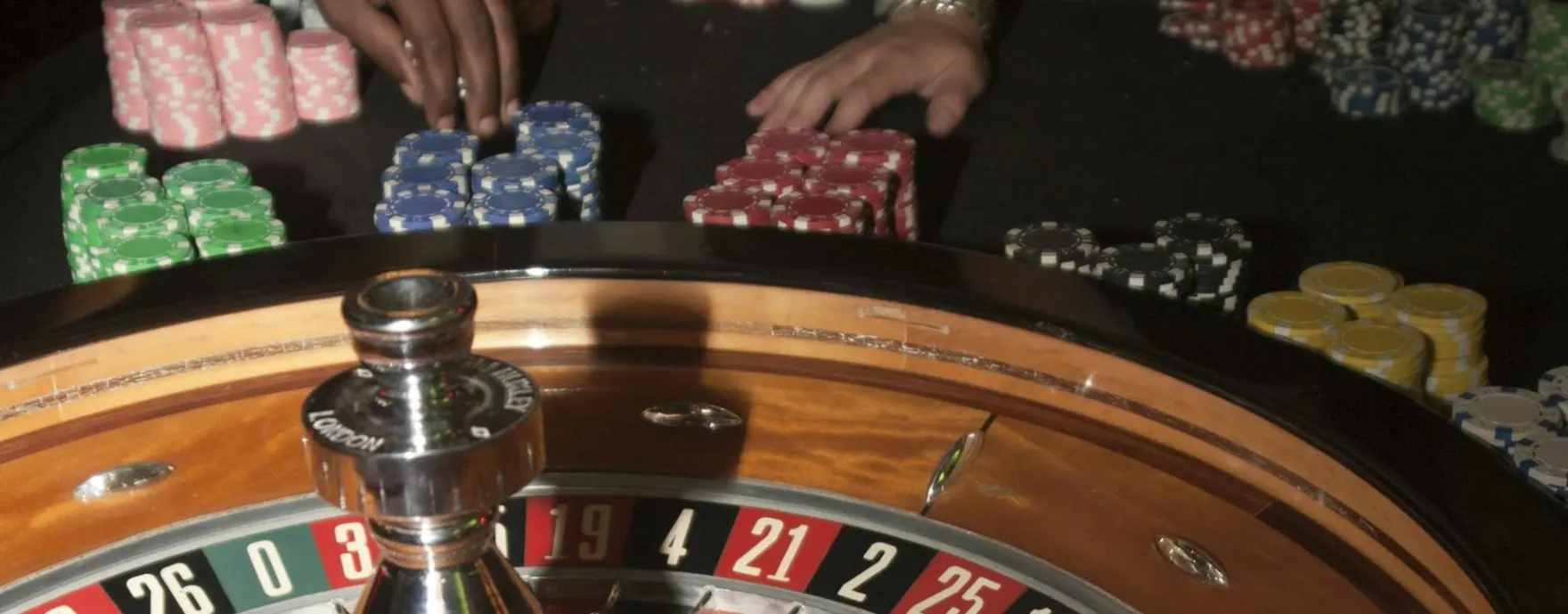 Mesa de casino en vivo de orobet con ruleta de madera, fichas de colores y crupier sobre fondo oscuro